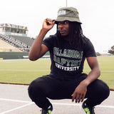 Person wearing an Oklahoma Baptist University shirt and a hat, squatting on a sports field.