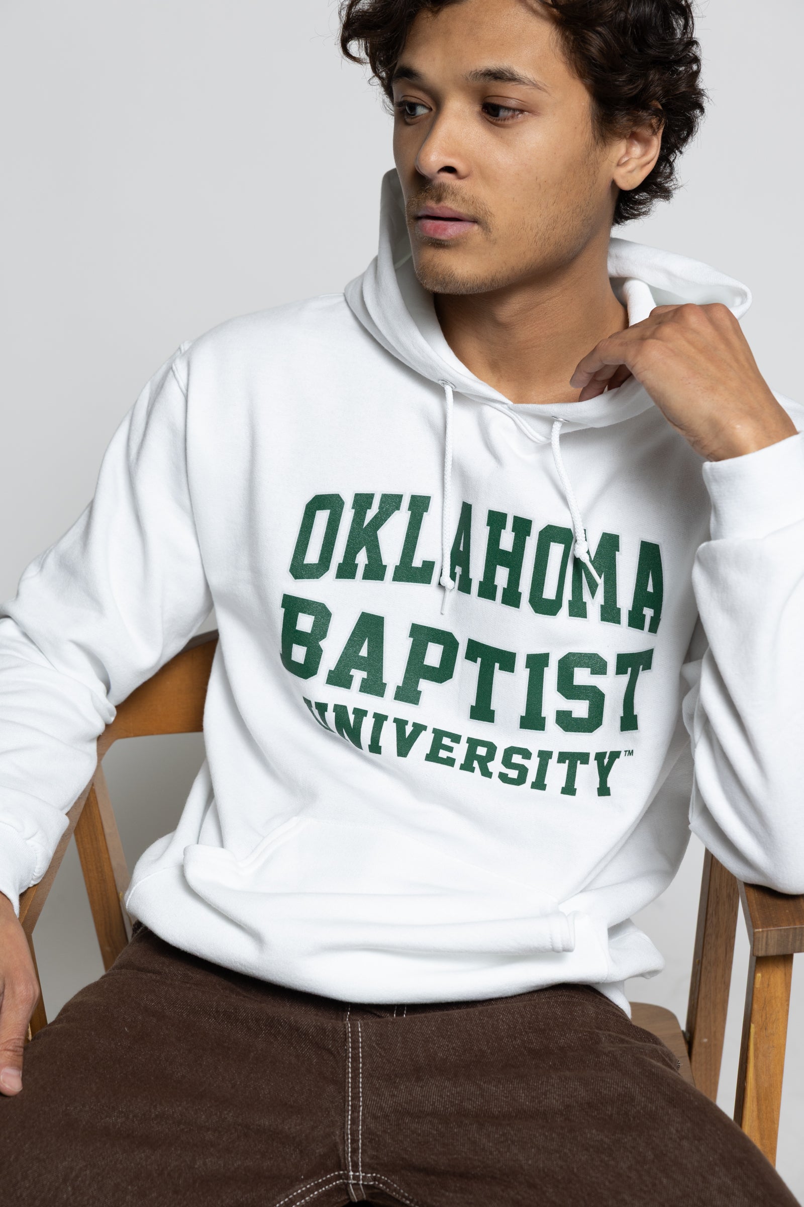Person wearing a white hoodie with 'Oklahoma Baptist University' text, sitting on a chair.